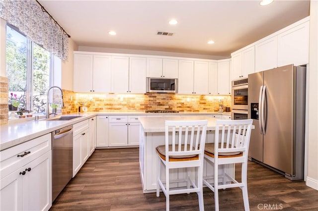 kitchen with a kitchen island, dark wood-style flooring, a sink, stainless steel appliances, and light countertops