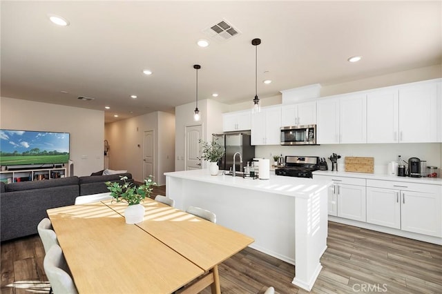 kitchen featuring a center island with sink, appliances with stainless steel finishes, wood finished floors, and recessed lighting