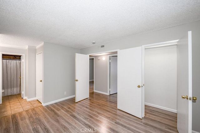 unfurnished bedroom featuring visible vents, a textured ceiling, baseboards, and wood finished floors