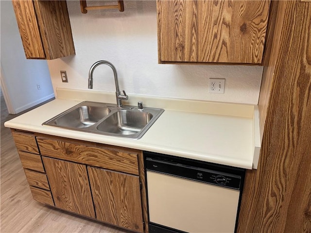 kitchen with a sink, light countertops, dishwasher, light wood finished floors, and brown cabinetry