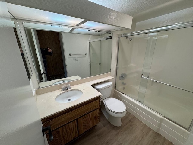 bathroom featuring enclosed tub / shower combo, a textured ceiling, toilet, wood finished floors, and vanity