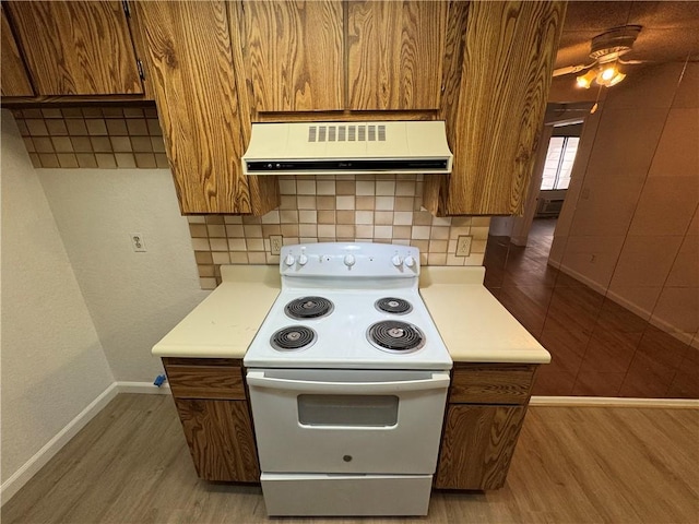 kitchen with electric range, brown cabinets, extractor fan, light countertops, and light wood-type flooring