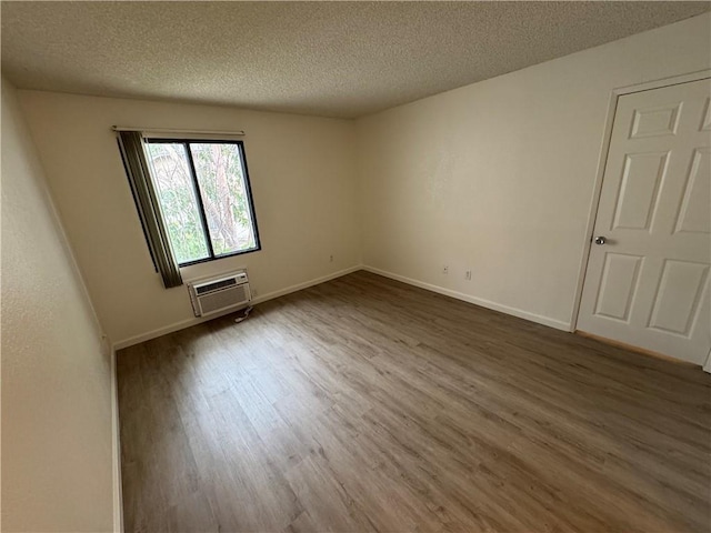 spare room featuring a textured ceiling, a wall mounted AC, wood finished floors, and baseboards