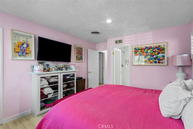 bedroom with visible vents, a textured ceiling, baseboards, and wood finished floors