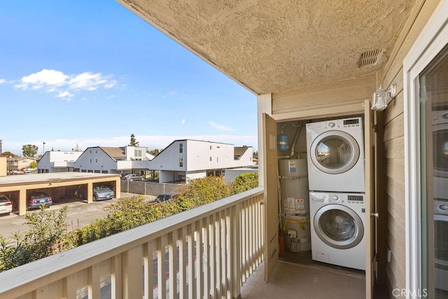 balcony featuring stacked washer / drying machine, strapped water heater, visible vents, and a residential view