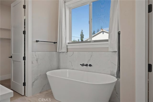 bathroom featuring marble finish floor, a freestanding bath, and tile walls