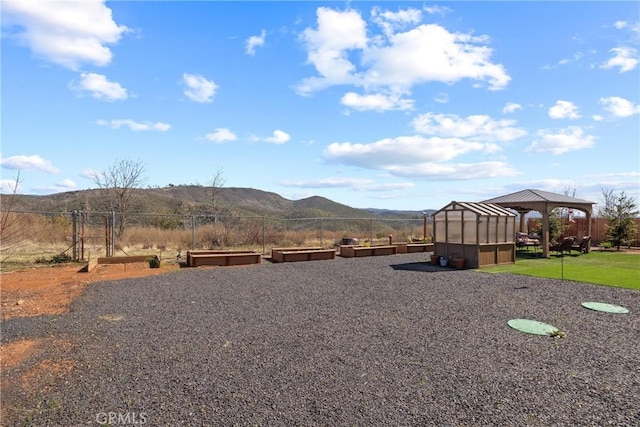 view of yard with a vegetable garden, a greenhouse, fence, an outdoor structure, and a mountain view