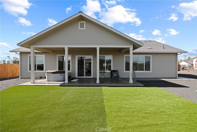 rear view of house featuring a patio, a shingled roof, fence, a yard, and a hot tub