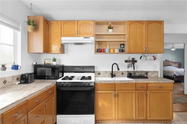 kitchen with tile counters, a sink, gas range, black microwave, and under cabinet range hood