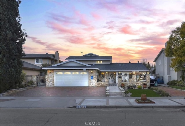 view of front of home with a garage, stone siding, a gate, fence, and decorative driveway