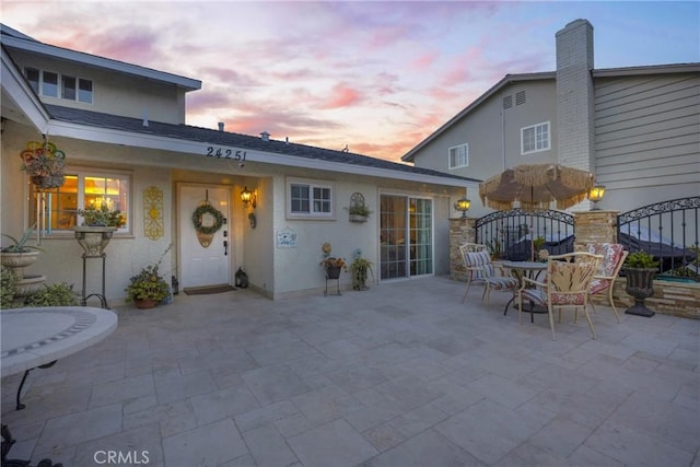 back of property at dusk featuring a patio area, a gate, and stucco siding