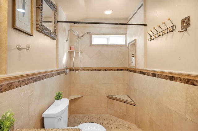 bathroom with toilet, a wainscoted wall, tile walls, and tiled shower