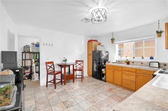 kitchen featuring tile counters, freestanding refrigerator, visible vents, and an inviting chandelier