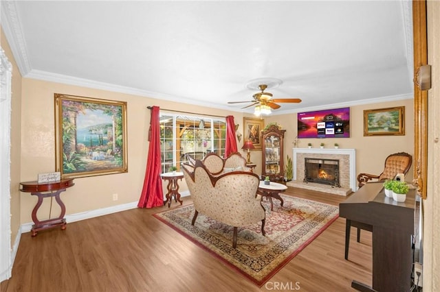 living area featuring a warm lit fireplace, baseboards, crown molding, and wood finished floors