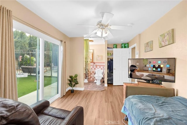 bedroom featuring a ceiling fan, baseboards, access to outside, light wood finished floors, and a walk in closet