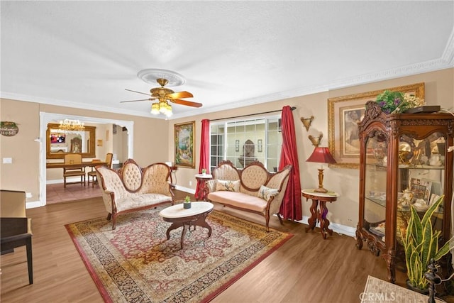 living room featuring baseboards, light wood finished floors, a ceiling fan, and crown molding