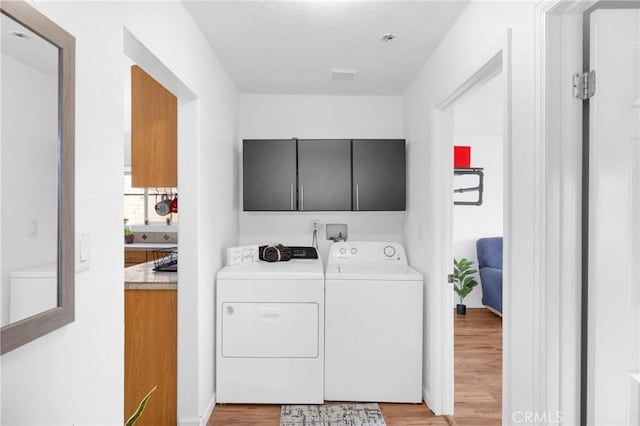 laundry area featuring light wood-style floors, washing machine and dryer, cabinet space, and visible vents