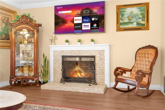 living area featuring baseboards, a stone fireplace, wood finished floors, and crown molding