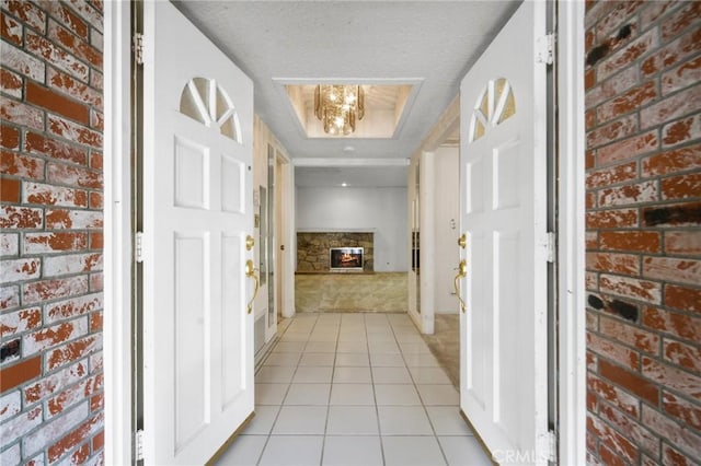 corridor featuring brick wall, a tray ceiling, and light tile patterned flooring