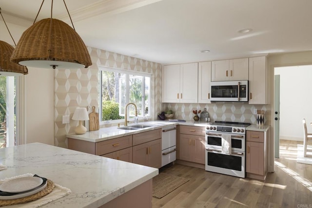 kitchen with light stone counters, a sink, light wood-style floors, backsplash, and double oven range