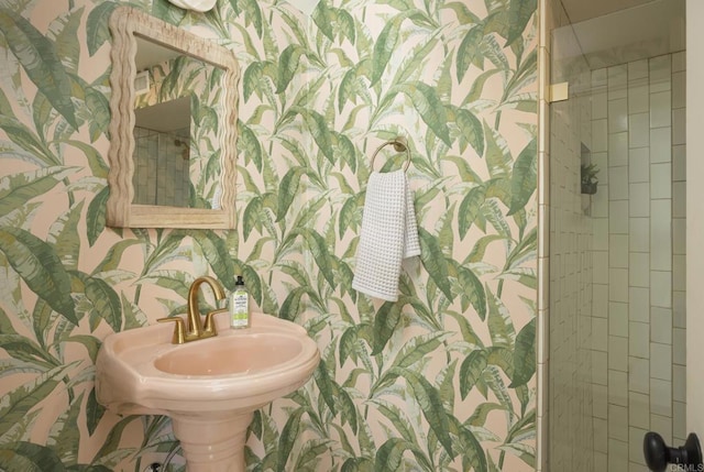 bathroom with a sink, wallpapered walls, and tiled shower