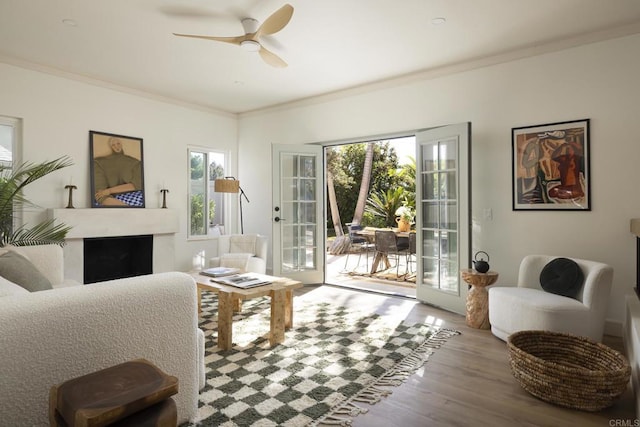 interior space featuring french doors, a fireplace, crown molding, a ceiling fan, and wood finished floors