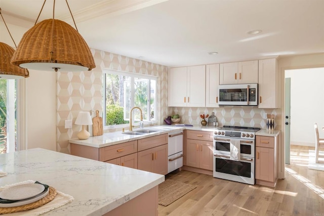 kitchen featuring decorative light fixtures, light wood finished floors, decorative backsplash, a sink, and double oven range