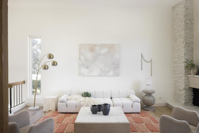 living area with baseboards, wood finished floors, and a stone fireplace