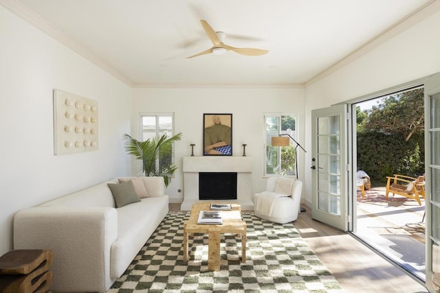 living room with ceiling fan, a fireplace, crown molding, and wood finished floors