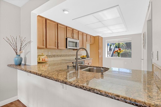 kitchen featuring backsplash, a sink, a peninsula, and light stone countertops