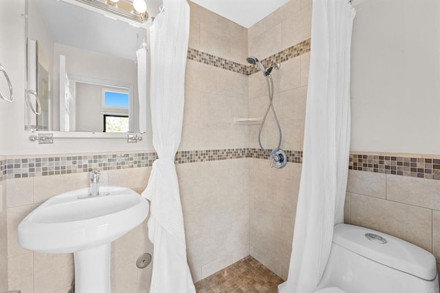 full bath featuring toilet, tiled shower, wainscoting, and tile walls