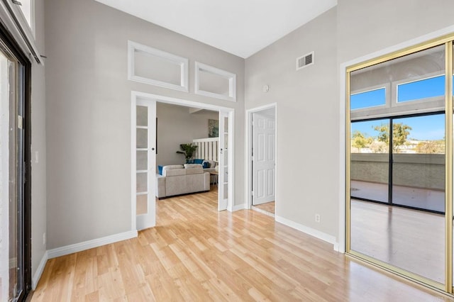 unfurnished room with a towering ceiling, light wood-style flooring, visible vents, and baseboards