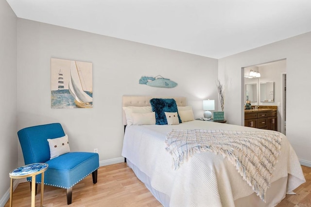 bedroom with light wood-type flooring, ensuite bath, baseboards, and a sink