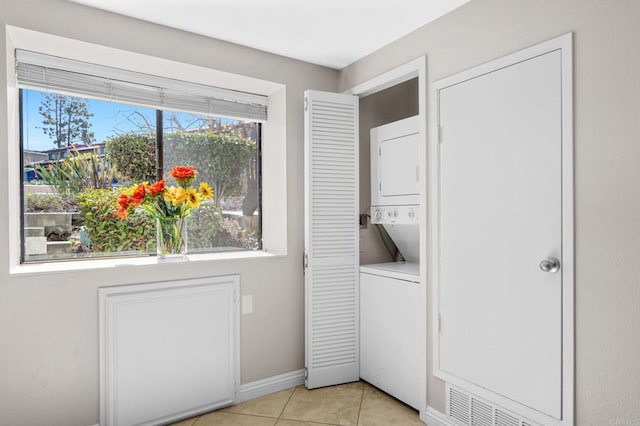 washroom with visible vents, light tile patterned flooring, stacked washing maching and dryer, laundry area, and baseboards