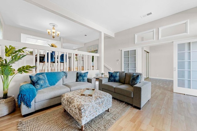 living area with visible vents, french doors, light wood-style floors, a chandelier, and beam ceiling