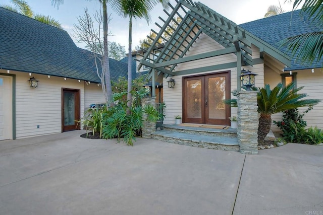 entrance to property featuring a shingled roof, french doors, and a pergola