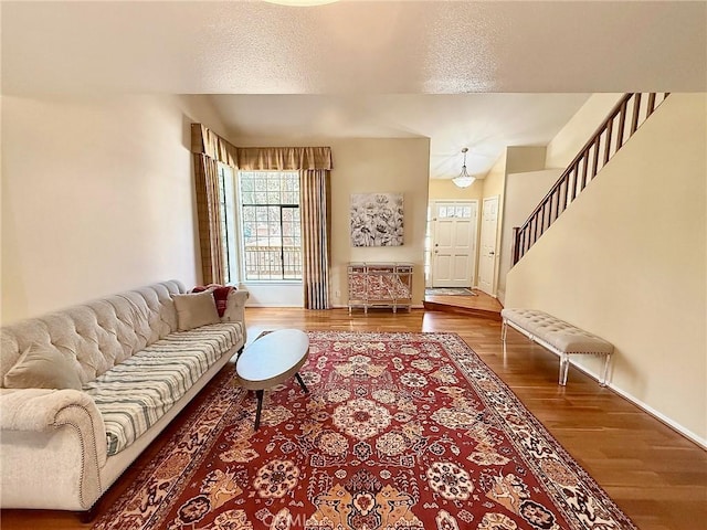 living area featuring a textured ceiling, wood finished floors, stairs, and baseboards