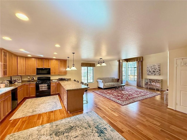 kitchen featuring light wood-style floors, glass insert cabinets, open floor plan, a peninsula, and black appliances