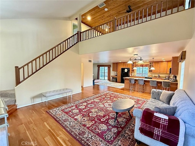 living room featuring visible vents, a towering ceiling, ceiling fan, stairway, and light wood-type flooring