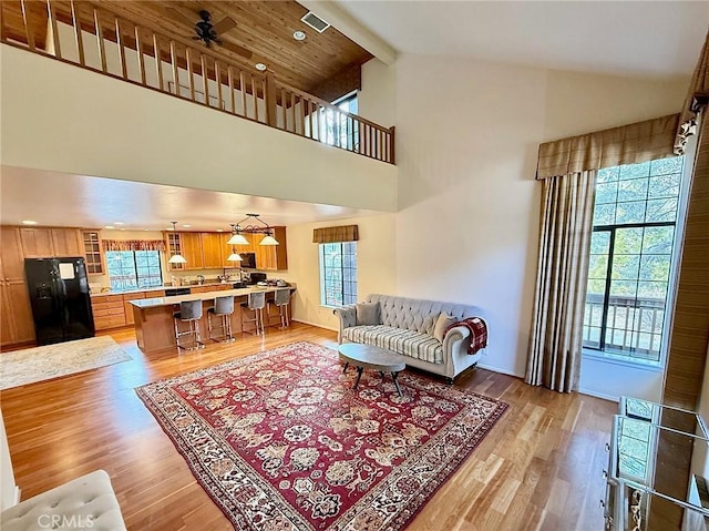 living area featuring high vaulted ceiling, plenty of natural light, beamed ceiling, and light wood-style flooring