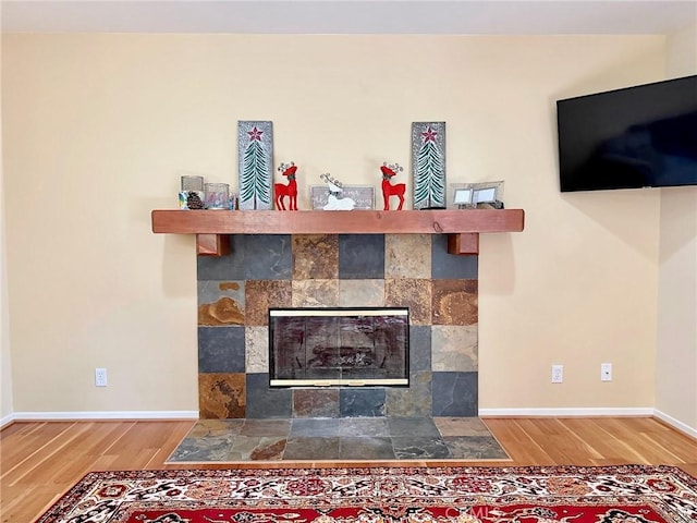 room details featuring a tiled fireplace, baseboards, and wood finished floors