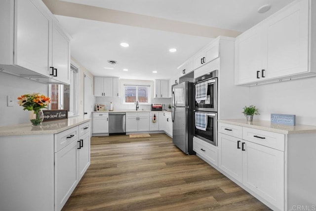 kitchen featuring recessed lighting, appliances with stainless steel finishes, white cabinets, a sink, and wood finished floors