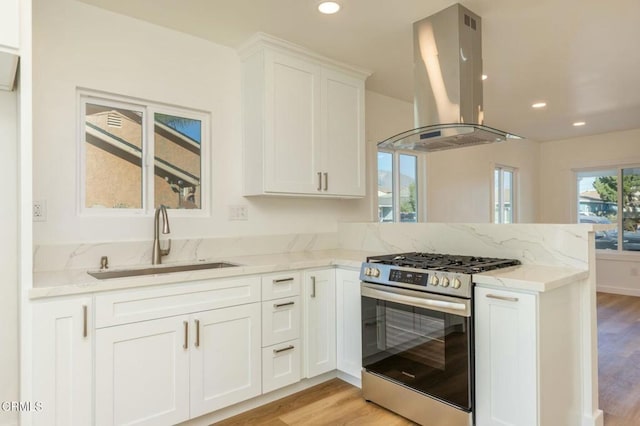 kitchen with a peninsula, stainless steel gas range, island exhaust hood, white cabinetry, and a sink