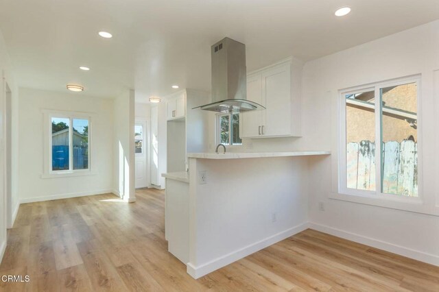 238 Stanford St, Santa Paula, CA 93060 - kitchen featuring island exhaust hood, light countertops, white cabinetry, a peninsula, and light wood-type flooring