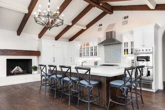 kitchen with stainless steel double oven, light countertops, a large island, decorative backsplash, and wall chimney exhaust hood