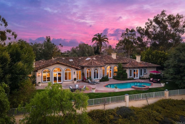 back of property at dusk with a pool with connected hot tub, french doors, a fenced backyard, and a patio