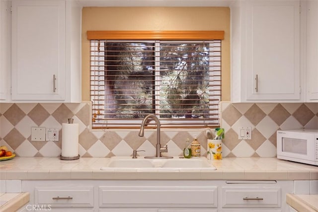 379 Avenida Castilla Unit Q, Laguna Woods, CA 92675 - kitchen featuring tasteful backsplash, white microwave, a sink, and white cabinets