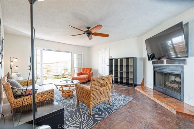 living room with a ceiling fan, a fireplace with raised hearth, and a textured ceiling