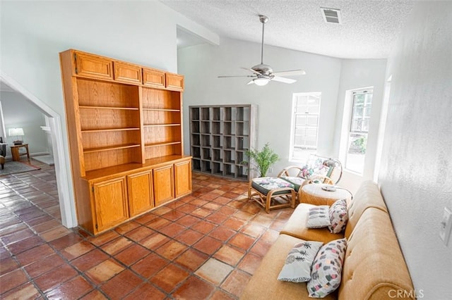 living area featuring vaulted ceiling with beams, ceiling fan, a textured ceiling, dark tile patterned flooring, and visible vents