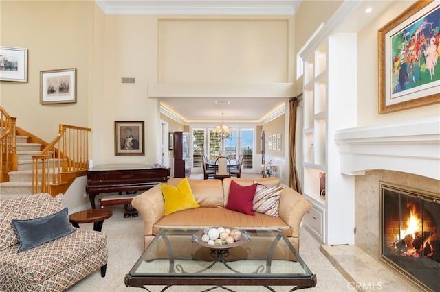 living area featuring carpet floors, an inviting chandelier, ornamental molding, a premium fireplace, and stairs